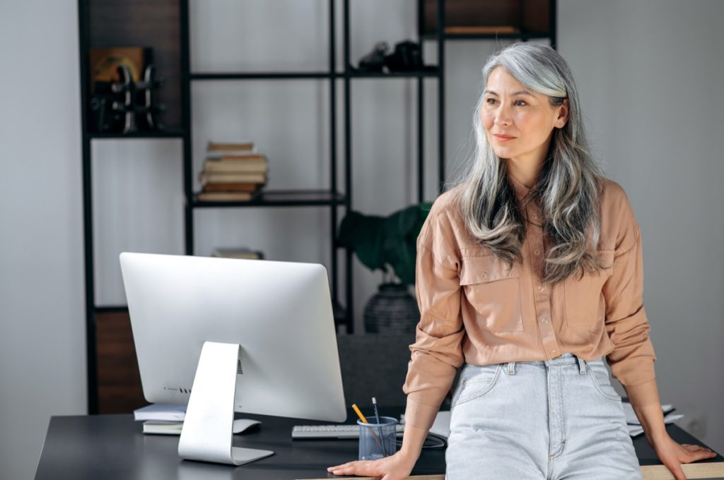 Woman with gray hair standing by her desk.