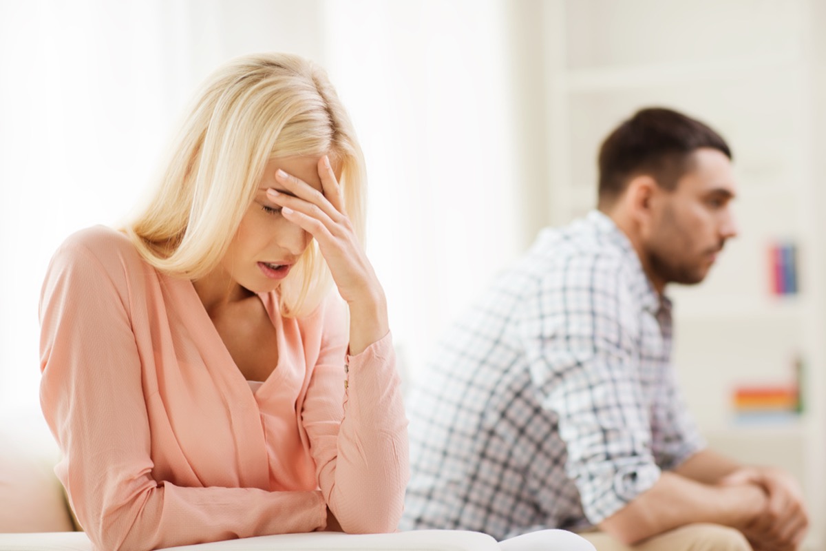 A woman in a pink sweater puts her hand on her head in annoyance at her partner.