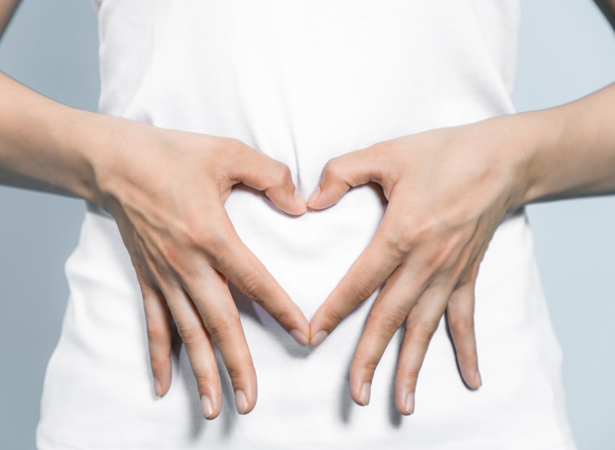 Closeup of a woman in a white t-shirt making a heart shape with her hands over her stomach