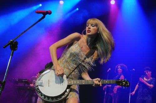 Taylor Swift wearing a. sequined dress playing the banjo.