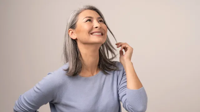 An attractive woman with gray hair wearing a lavender sweater looking up and smiling.