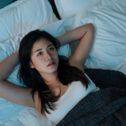 young asian woman lying in bed looking worried and can't fall asleep