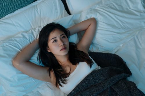 young asian woman lying in bed looking worried and can't fall asleep