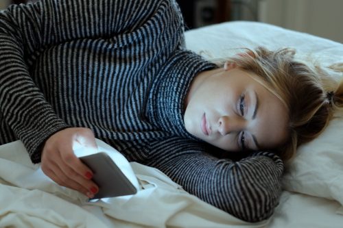 girl holding mobile phone while laying on bed in a bedroom