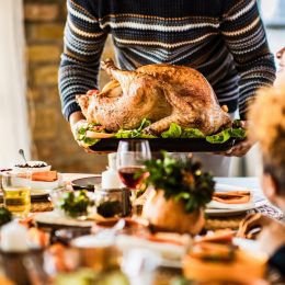 A person placing a Thanksgiving turkey down on the table in front of their family