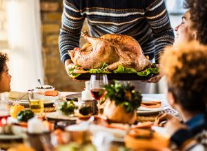 A person placing a Thanksgiving turkey down on the table in front of their family