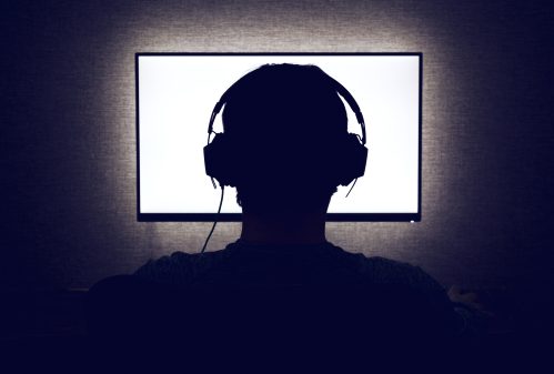 silhouette of man in front of a computer screen wearing headphones
