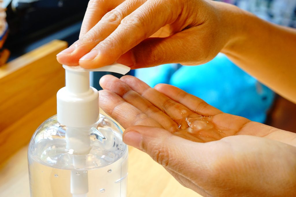 A close up of a person putting gel hand sanitizer into their palm with a pump bottle