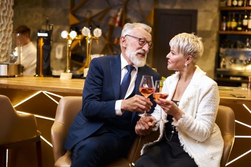A well-dressed older couple clinking wine glasses at a chic bar.