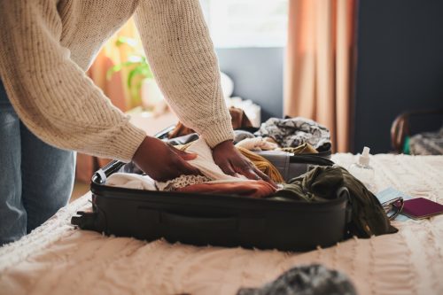 Ảnh chụp một người phụ nữ không rõ danh tính đang đóng gói hoặc mở đồ đạc của mình vào vali ở nhà trước khi đi du lịch
