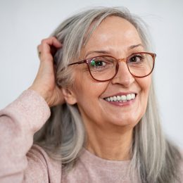 A senior woman wearing a light pink sweater and glasses touching her gray hair.