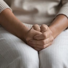 Close up of a woman's hands nervously clenched in her lap.