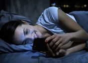 Young woman smiling on her phone in bed