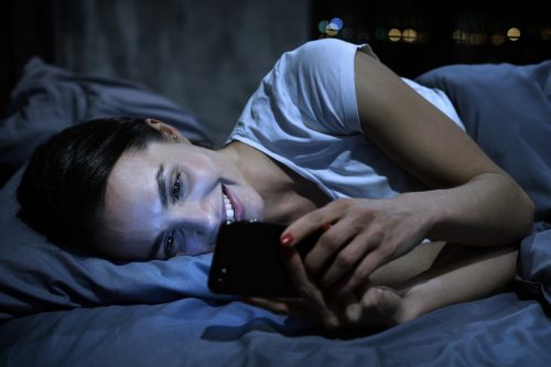 Young woman smiling on her phone in bed