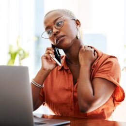 A young woman talking on the phone with a concerned look on her face while sitting in front of a laptop