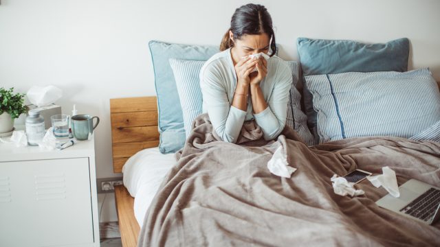 A woman lying in bed sick with the flu blowing her nose