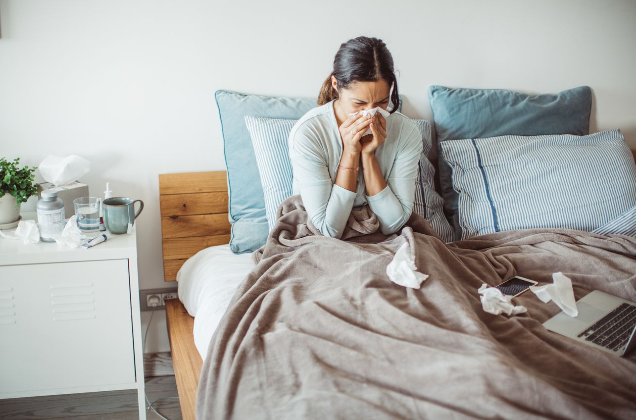 A woman lying in bed sick with the flu blowing her nose