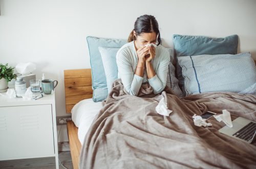 A woman lying in bed sick with the flu blowing her nose