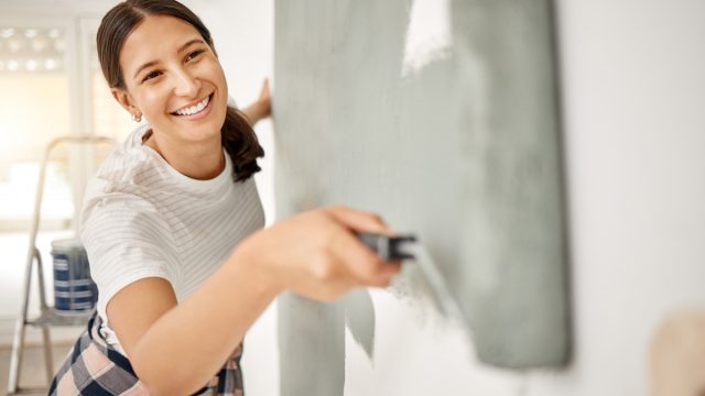Close up of a young woman rolling gray-green paint on the wall.