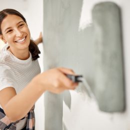 Close up of a young woman rolling gray-green paint on the wall.