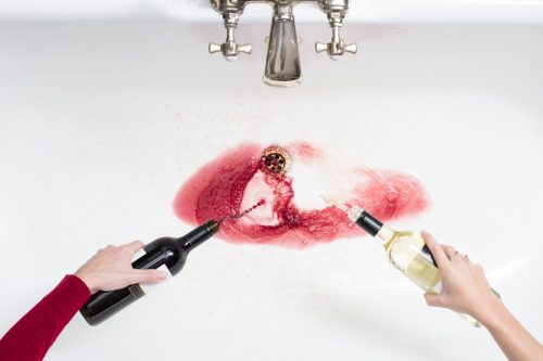 Two hands pouring wine down a sink