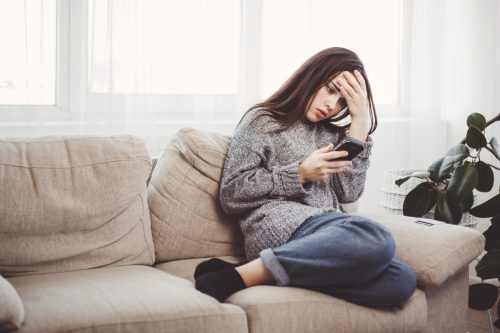 Upset woman sitting on her couch looking at her text messages.