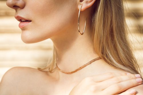 Close-up of a beautiful young blonde woman's neck with gold earrings and a gold choker.