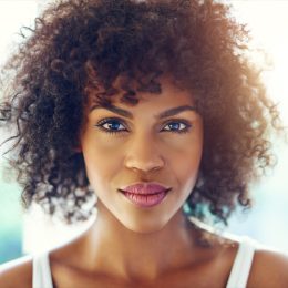 Portrait of young afro-american pretty girl looking at camera on blurred inside background.