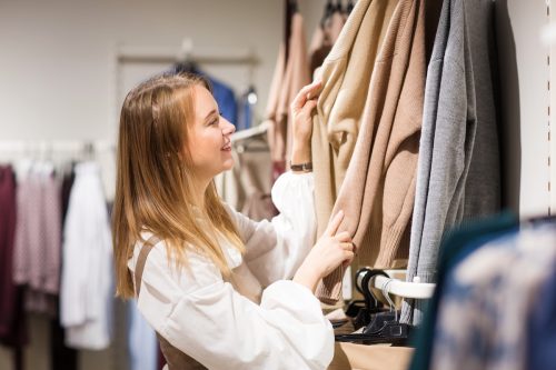 A young woman smiling and looking at sweaters in a store.
