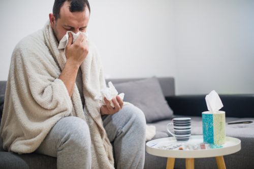 Sick man wrapped in blanket blowing his nose