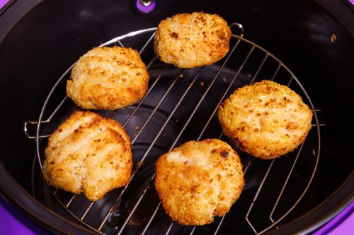 cooked chicken meatballs in breadcrumbs on steel grille in opened airfryer - close-up