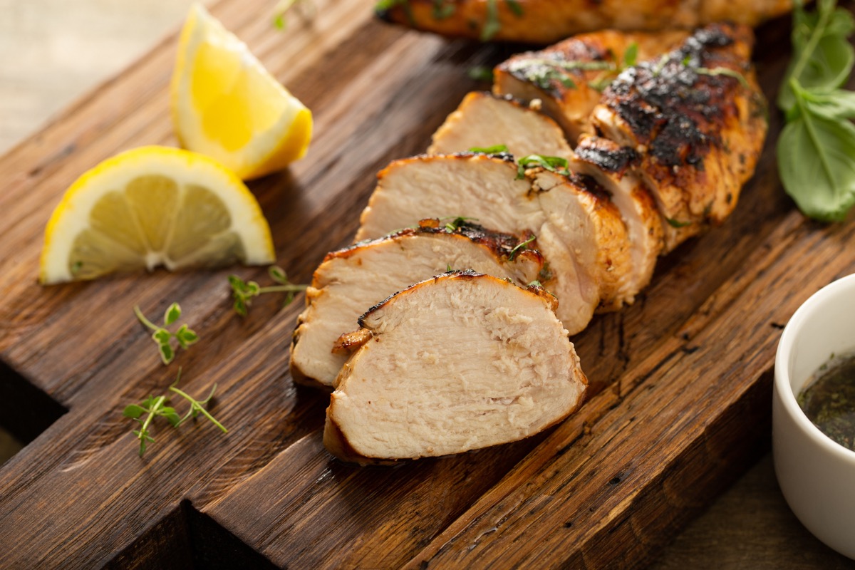 Balsamic grilled chicken breast with fresh herbs sliced on a rustic wooden board