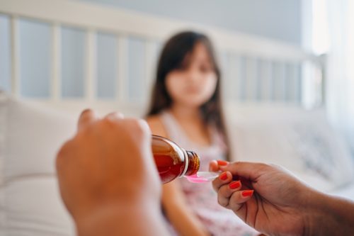 Hands of mom pouring cough syrup medicine into clear spoon to daughter