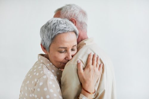 Elderly woman with grey hair enjoying the dance with her husband against the white background