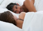 A couple looking at each in bed, with the man's face shown smiling.