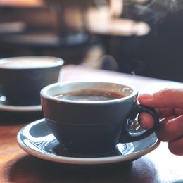 A closeup of two cups of coffee on a table top with a hand reaching for one