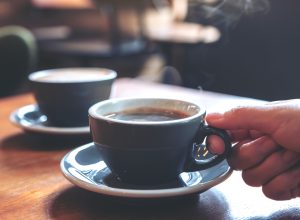 A closeup of two cups of coffee on a table top with a hand reaching for one