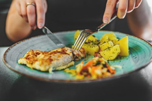 woman hand holding fork and knife eat chicken breast meat with potato in a plate