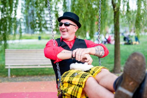An eccentric-looking middle-aged man wearing a plaid skirt on a children's swing.