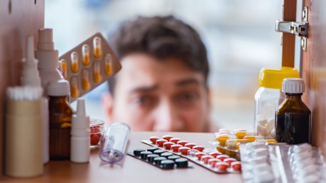 Sick ill man looking for medicines at pharmacy shelf