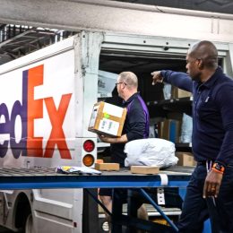 Two FedEx employees sorting packages onto a truck