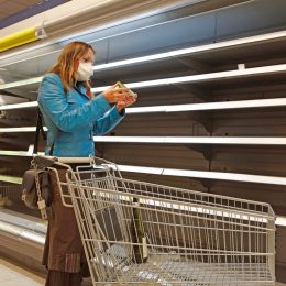 Shopping woman with respirator mask looking for some food at empty shelves in the supermarket