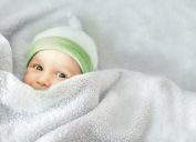 gender-neutral baby in a green hat and under covers