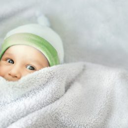 gender-neutral baby in a green hat and under covers