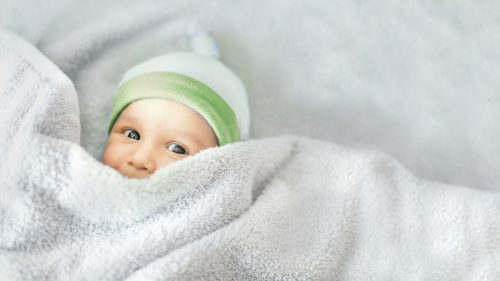 baby in a green hat and under covers