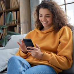 Woman in a yellow sweater on her iphone smiling.