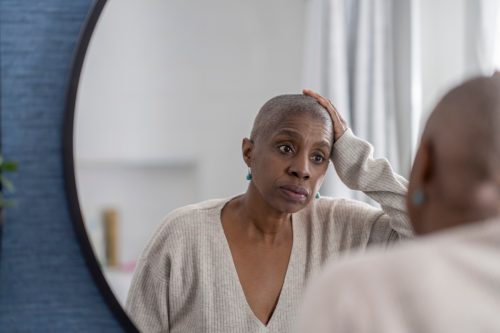An elderly woman ponders in the mirror and admires her newly shaved hair.