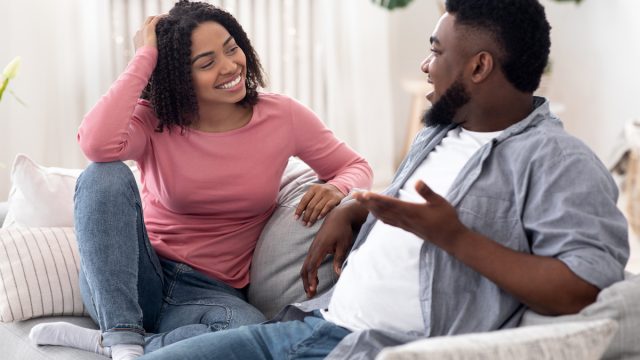 A happy young couple sitting on the couch in jeans and talking.