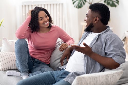 A happy young couple sitting on the couch in jeans and talking.