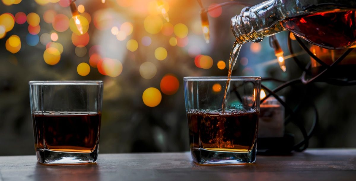 A glass of whiskey on wooden bar with holiday lights behind it